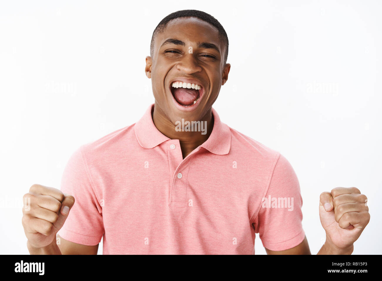 Close-up shot of charismatic over-emotive and excited young happy african american man clenching fists in joy and cheer yelling yes from cheerful feelings being glad to win and be champion Stock Photo