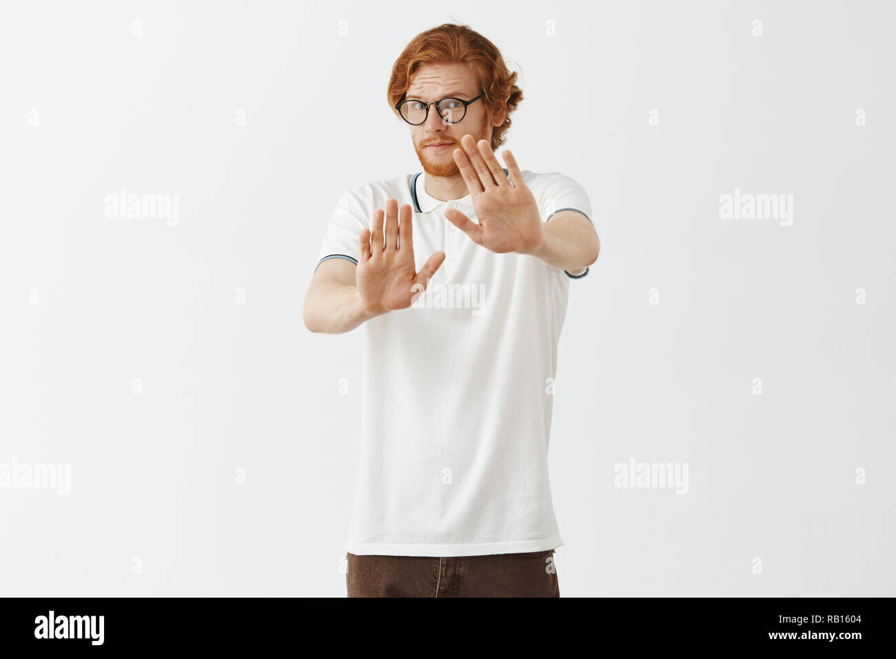 Man pulls hands towards camera to restrain from something dangerous. Intense worried guy showing stop or rejection gesture with raised hands pursing lips and frowning unwilling something happen Stock Photo