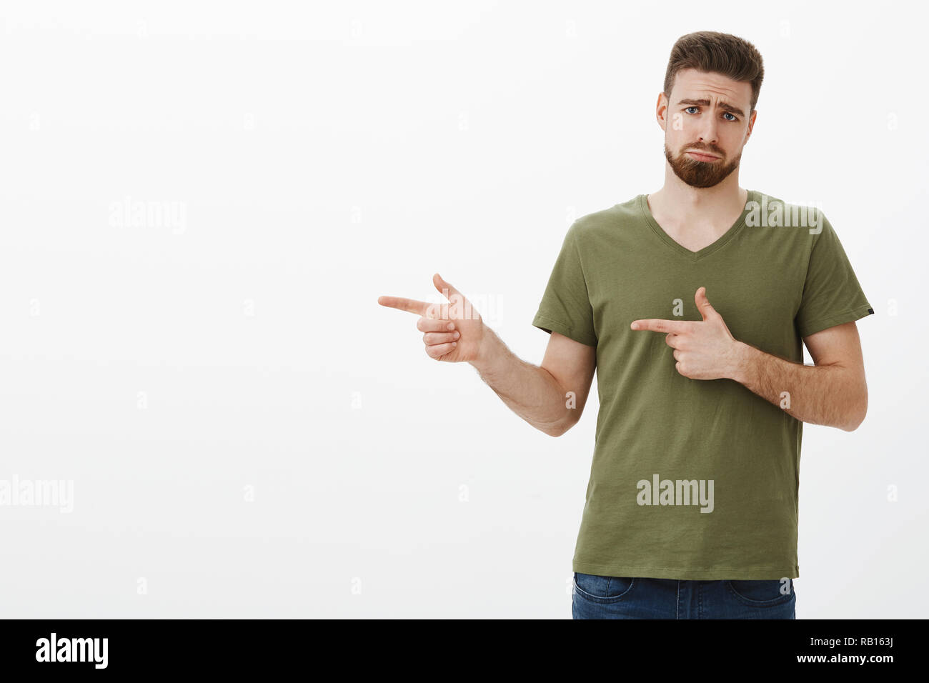 Cute unhappy and upset boyfriend pouting and frowning like gloomy puppy as pointing left disappointed and jealous of not having awesome product as present of valentines day over white wall Stock Photo