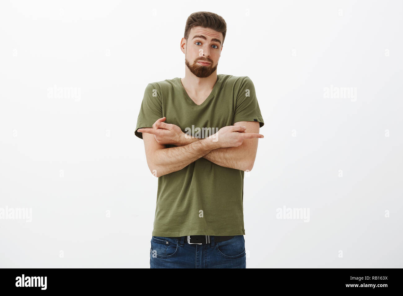 Help me make decision I not know. Portrait of confused and unsure, hesitant cute male customer with beard picking gift for valentines day cross hands and pointing sideways uncertain, asking advice Stock Photo