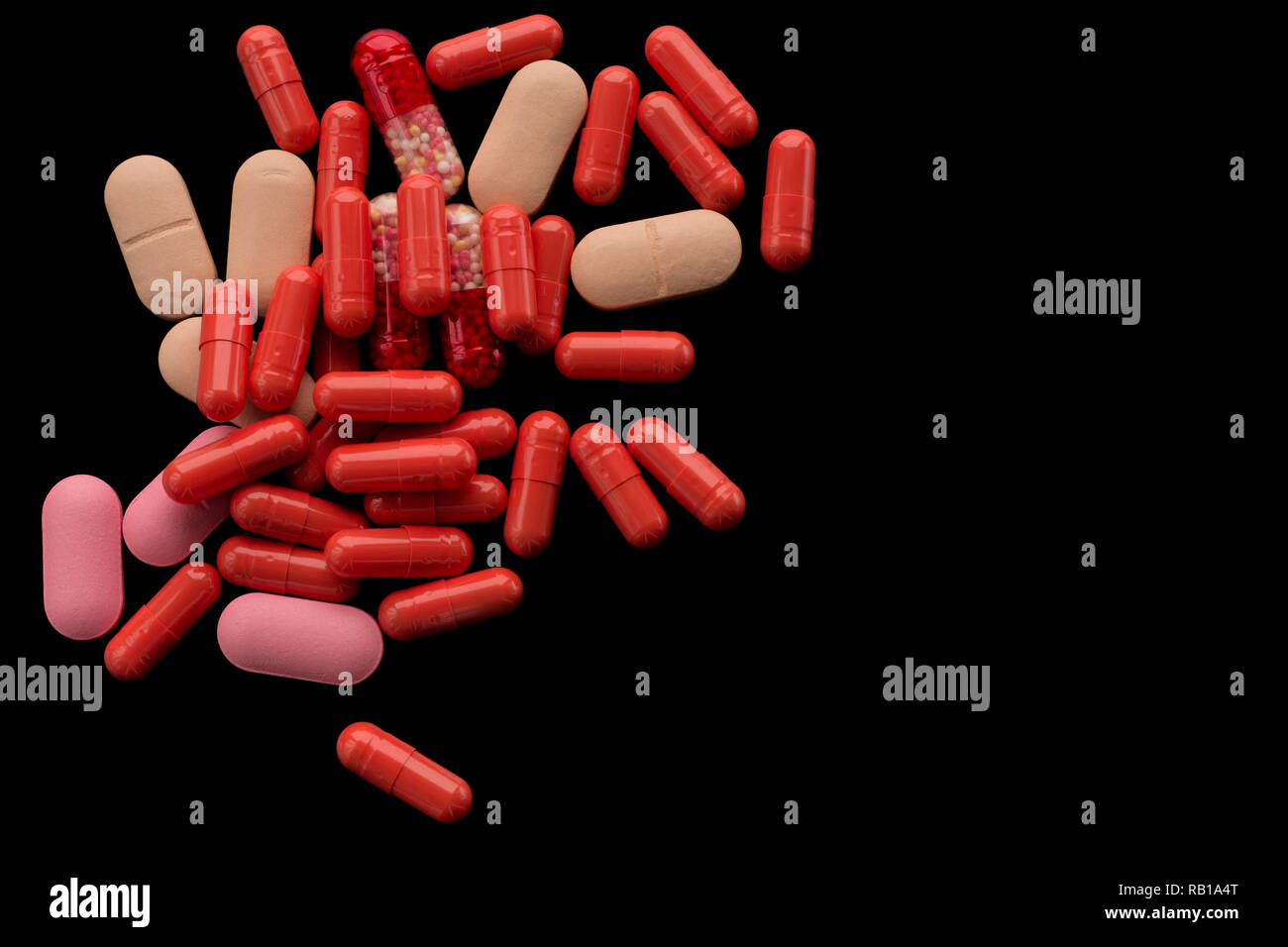 A pile of red, beige, pink tablets, pills or capsules on the black background. For medical, pharmaceutical topics, health care Stock Photo