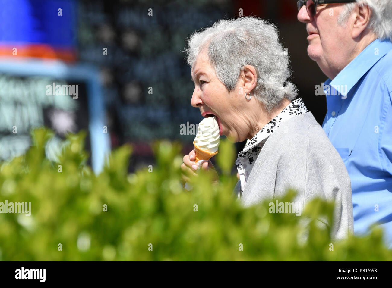 Senior couple walking on a promenade on a warm Spring day in the UK, eating ice creams. Stock Photo