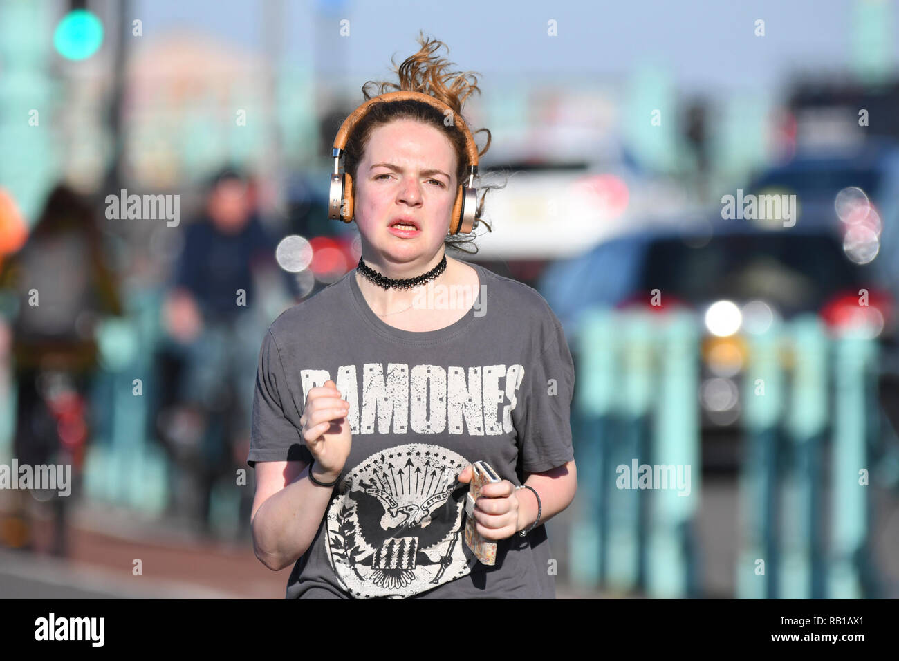 Young woman jogging towards camera wearing headphones, looking hot and sweaty. Stock Photo