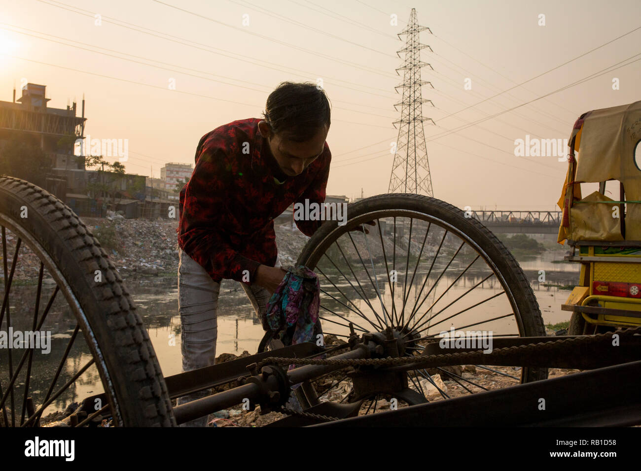 DHAKA, BANGLADESH - JANUARY 05 : A rickshaw puller repair his rickshaw on the Buriganga river in Dhaka, Bangladesh on January 05, 2019. The chemical waste of mills and factories, household waste eventually makes the Buriganga River miserable, which is considered to be Dhaka's lifeline.  Thousands of people depend on the river daily for bathing, washing clothes, irrigation of food and transportation of goods. The river has suffered extreme biodiversity loss and has now turned narrow. A large swathe of the Buriganga River, which is the lifeline of the capital, has turned pitch-black with toxic w Stock Photo