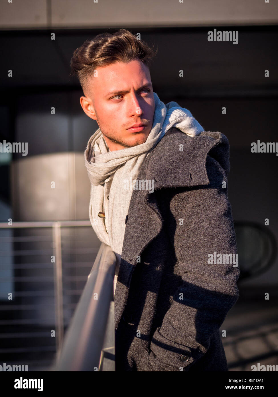 One handsome young man in urban setting in moden city, standing, wearing black coat and scarf in winter day Stock Photo