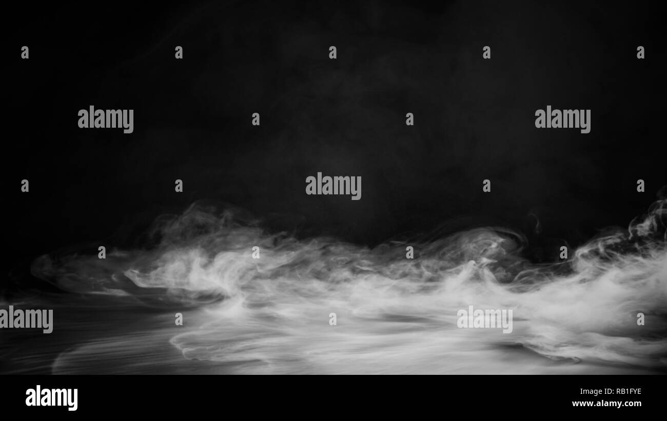 Rolling billows of smoke mist clouds from dry ice across the bottom light . Fog on floor isolated background black texture Stock Photo