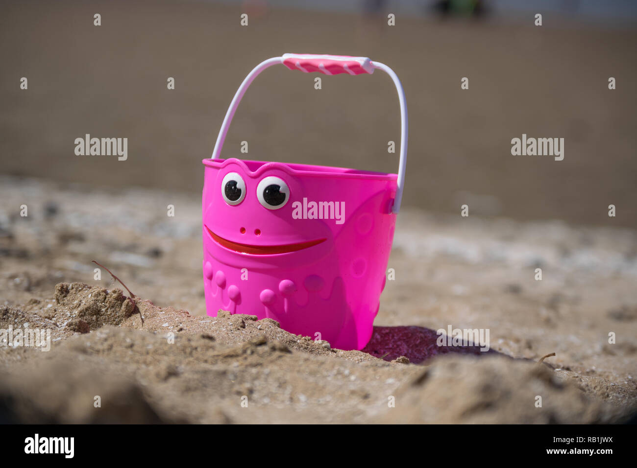 A Pink Bucket with a Smiley face sitting on a beach Stock Photo