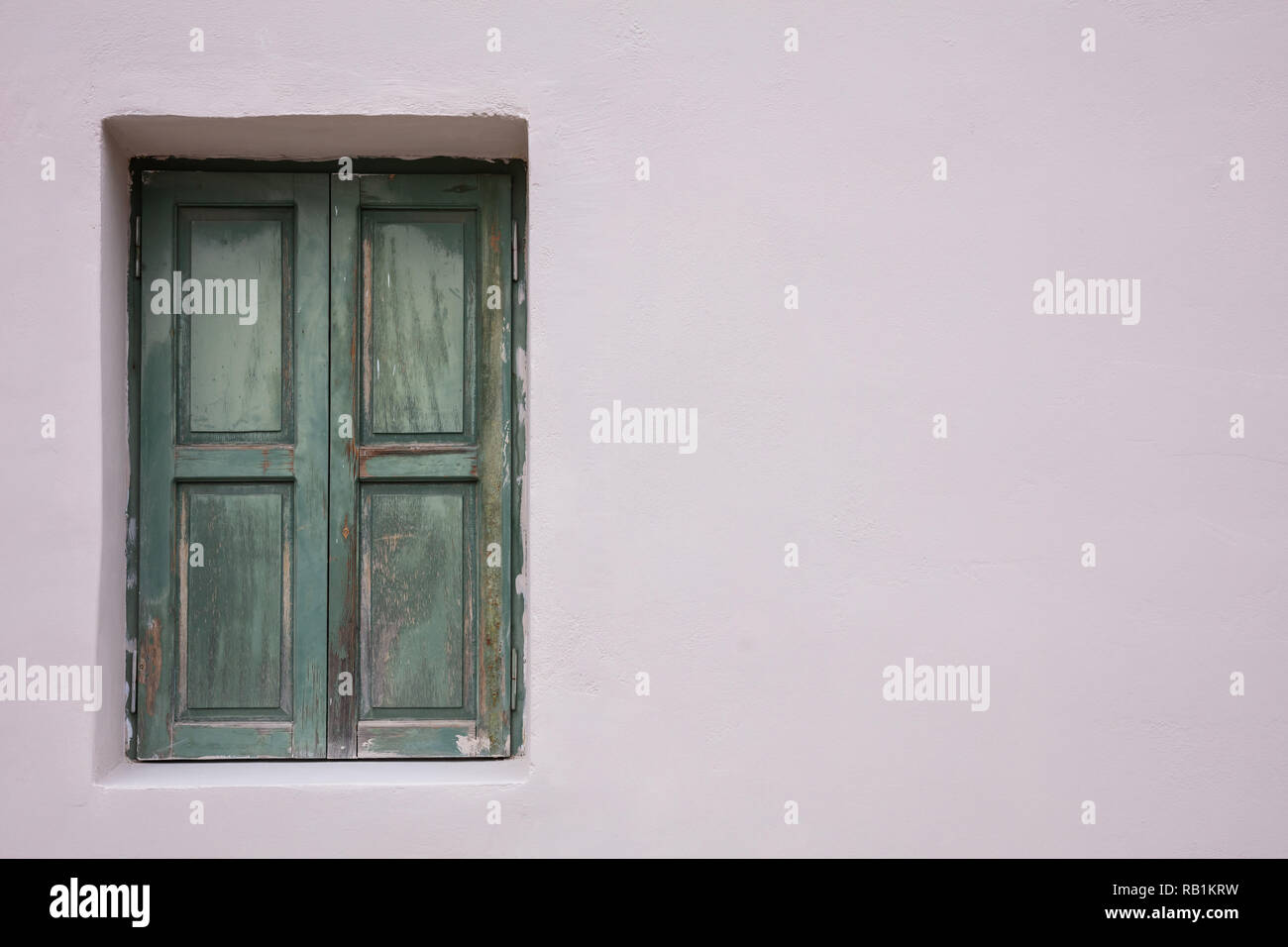 Old fashioned worn window with green wooden shutters, closed, on painted wall background. Traditional house facade, old town of Plaka, Athens Greece Stock Photo