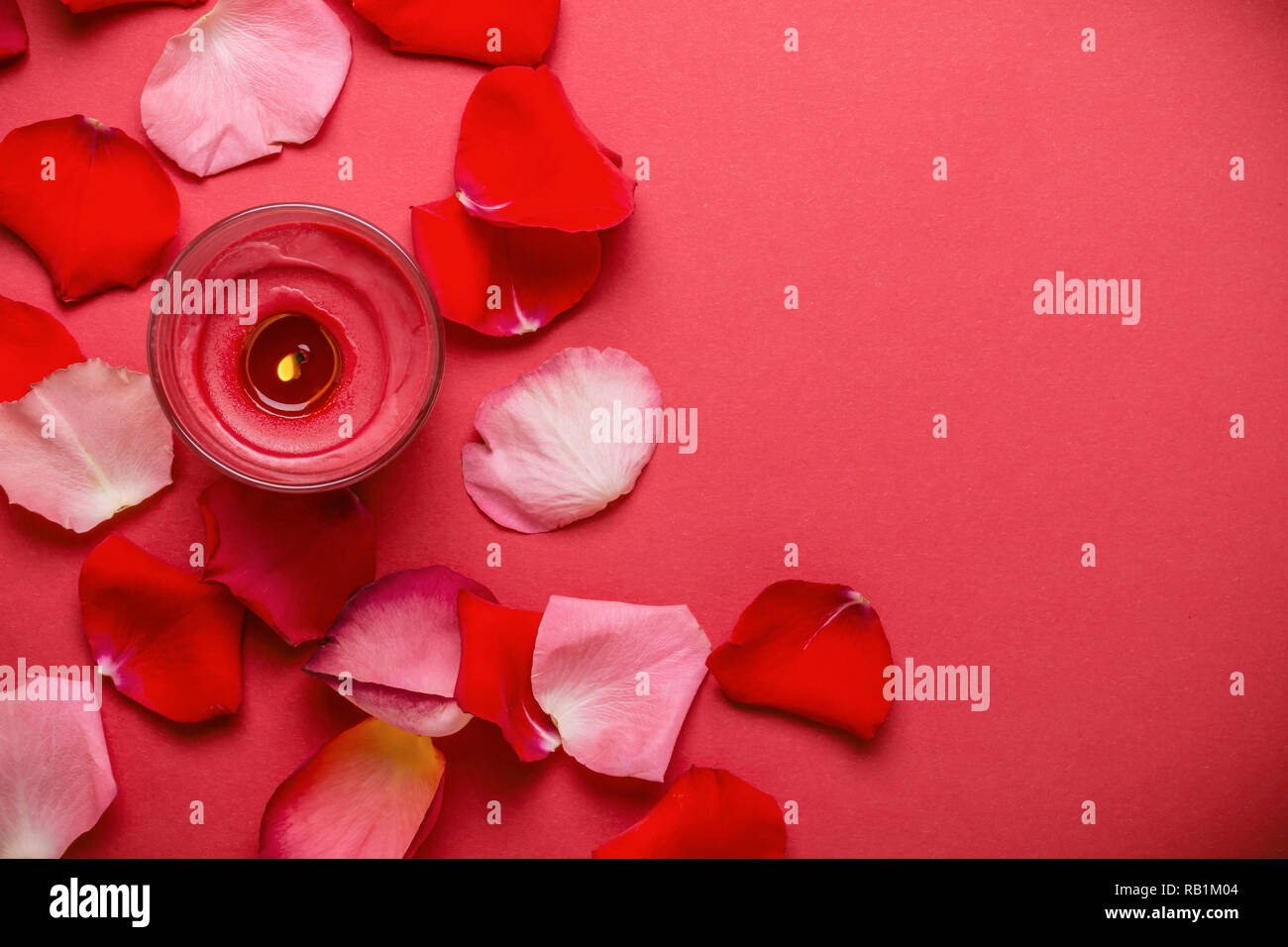 Candle and rose petals on red background. Stock Photo