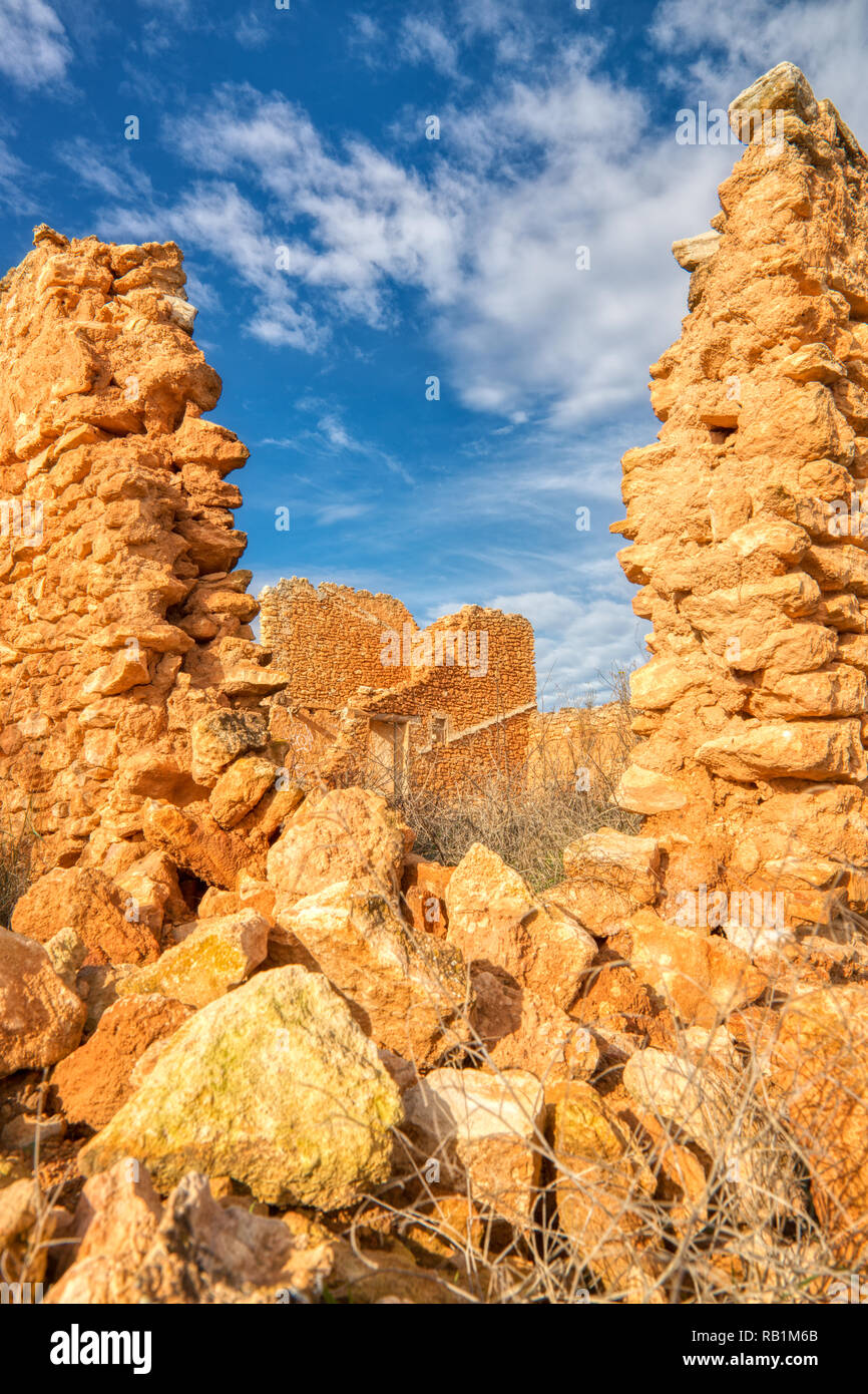 A vertical photo of the ruins of an old stone house looking through a broken part of the wall at another part of the house with a blue sky and clouds Stock Photo
