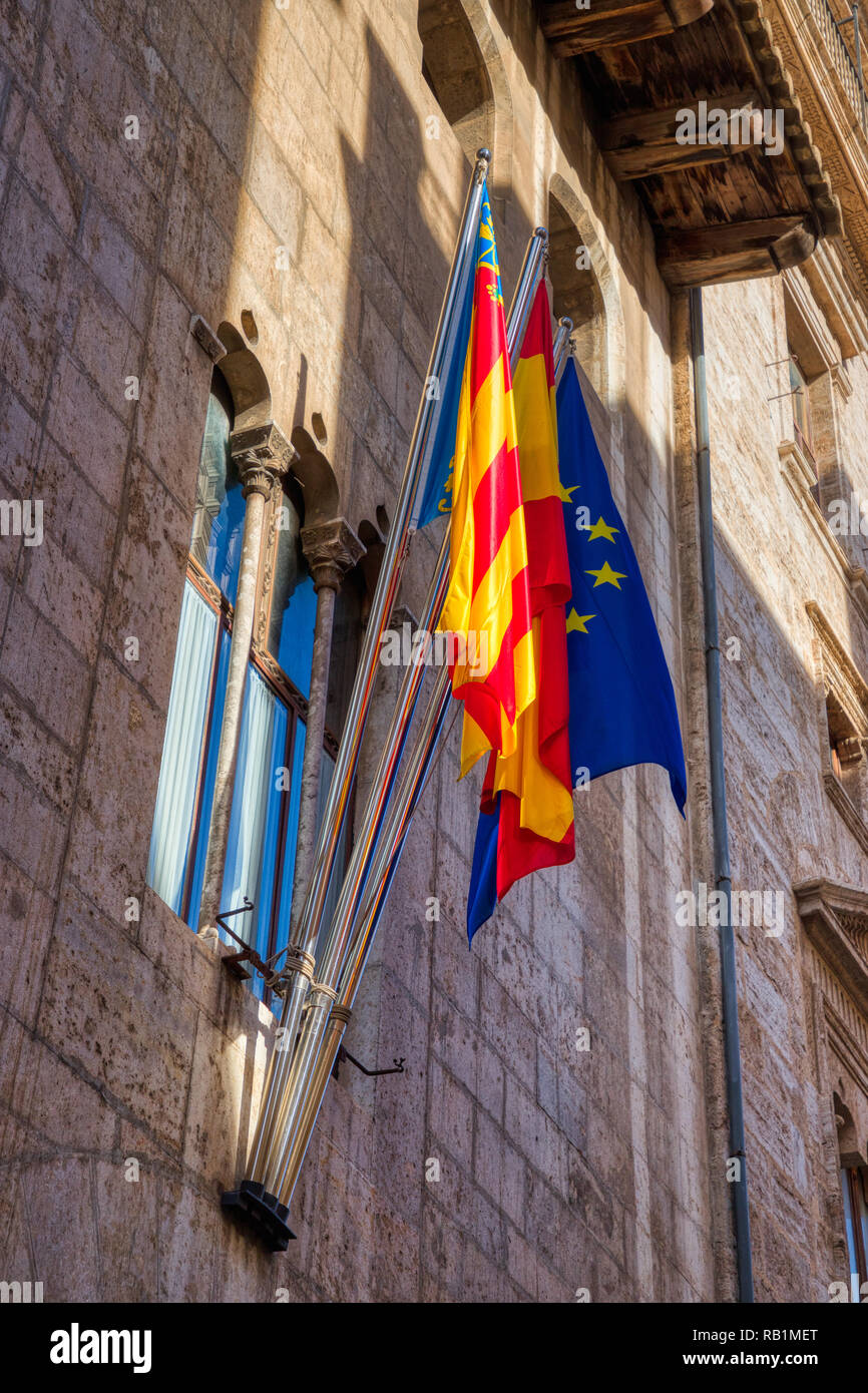A vertical photo of the bright red, yellow and blue EU, Spanish and Valencian flags hanging outside an old stone building in Valencia Stock Photo