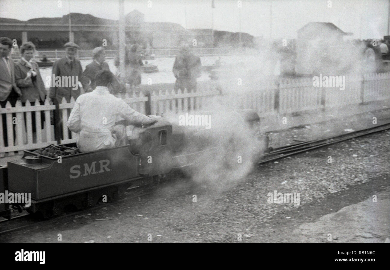 1950s, steam arises from a minature steam (SMR) locomotive on the minature railway at Southsea, Portsmouth, England, UK. The Southsea Minature railway first opened in 1932 as a 9.5' guage and after the war reguaged to 10 1/4' and became a huge success with many thousands of visitors. In 1951 a company called 'Southen Miniature Railways'  (SMR) took over the operation of the line and one of it's locos with engine driver on the track can be seen in the picture, Stock Photo