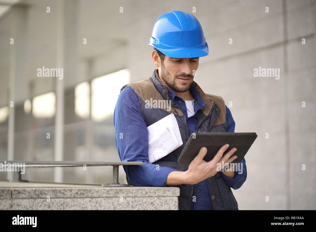 Handsome building expert in hardhat outdoors with tablet and blueprint ...