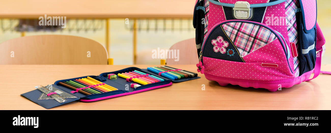 Pink girly school bag and pencil case on a desk in an empty classroom