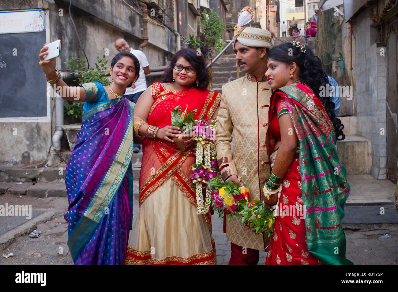 A friend of a newly wed couple in a backyard in Walkeshwar area, Mumbai, India, takes a photo on her mobile, a man in the b/g duly acting along Stock Photo
