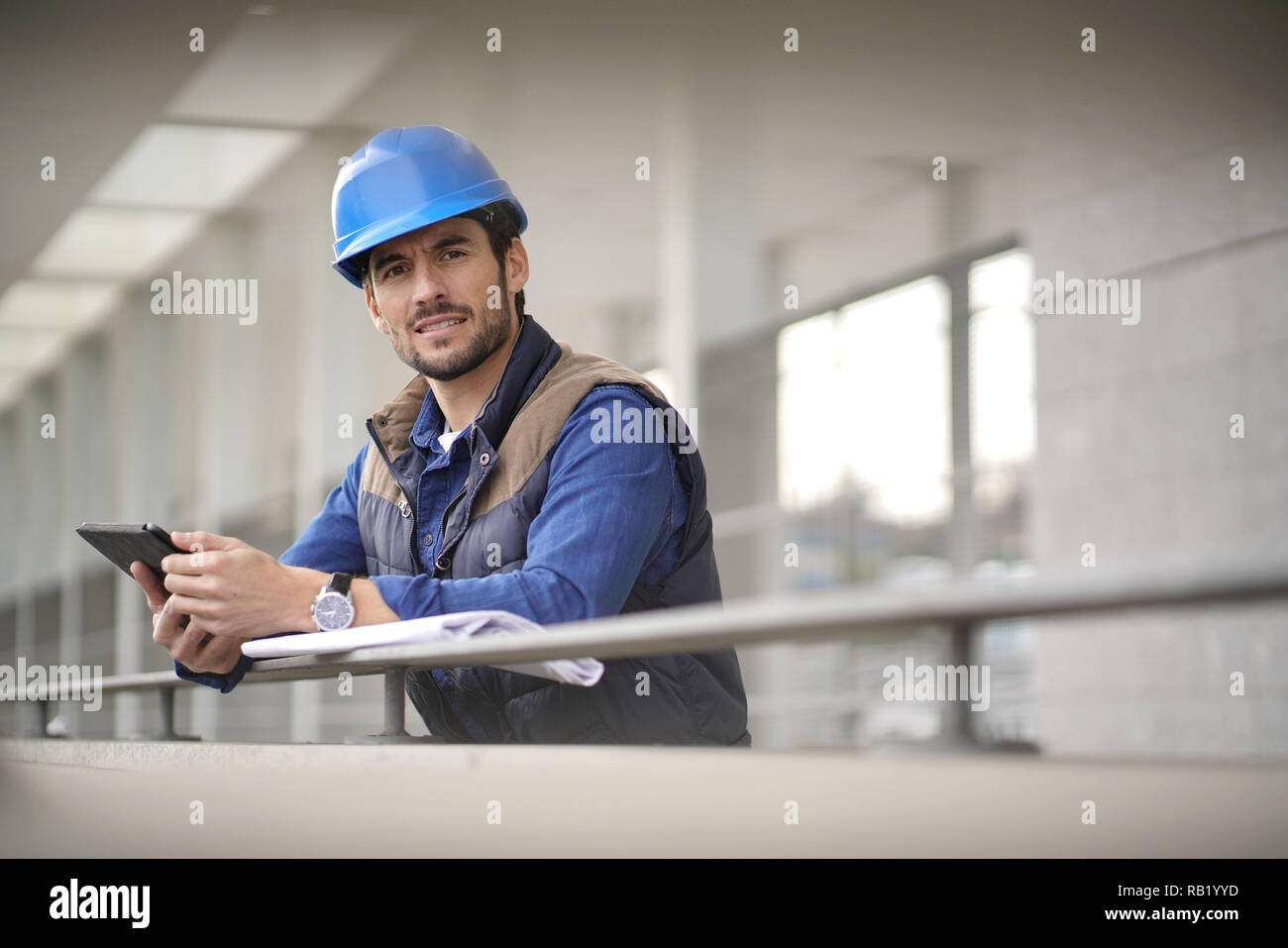Handsome building expert in hardhat outdoors with tablet and blueprint ...