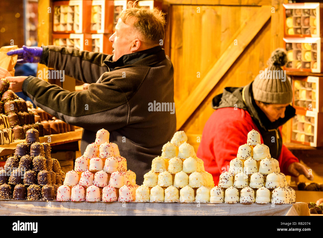 People working on Christmas Market stall, selling chocolates (varieties of chocolate teacakes displayed on counter & in boxes) - York, England, UK Stock Photo