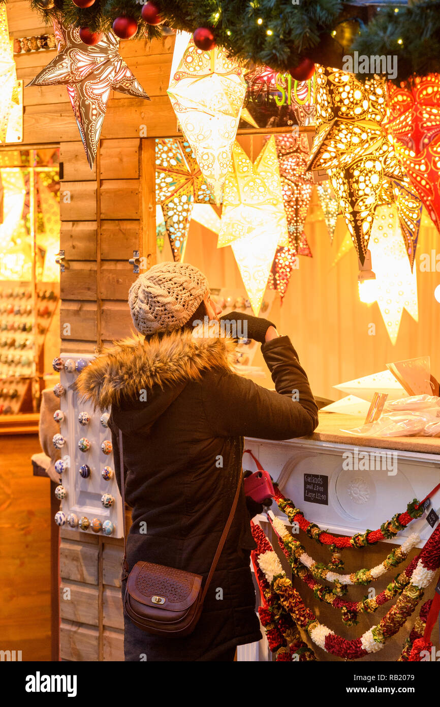 Woman at Christmas Market stall (potential customer) looking at paper star lights (lanterns) on display, casting warm golden glow - York, England, UK. Stock Photo