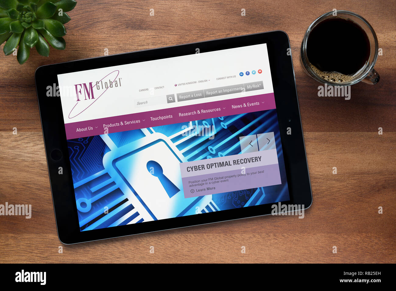 The website of FM Global is seen on an iPad tablet, on a wooden table along with an espresso coffee and a house plant (Editorial use only). Stock Photo