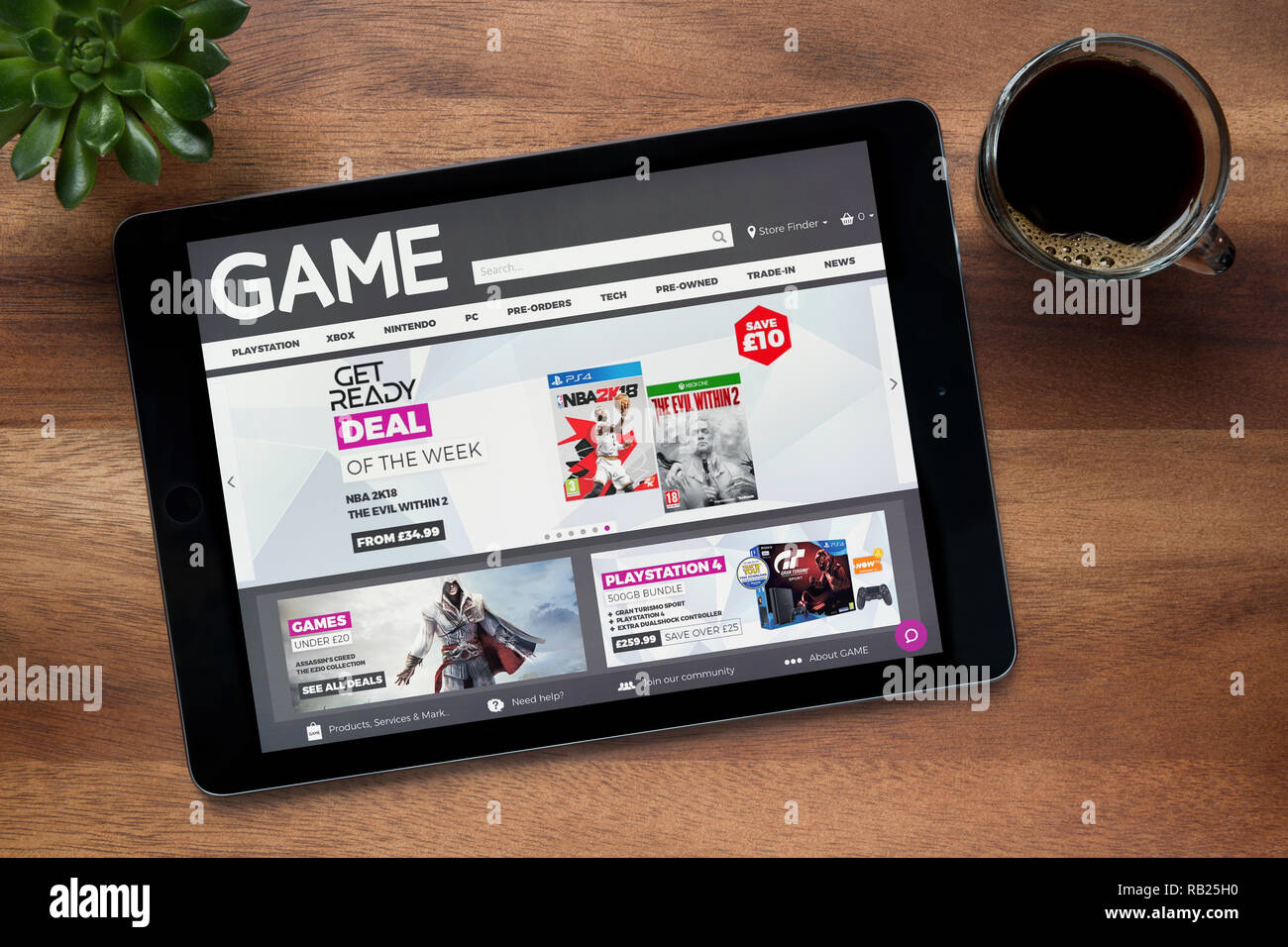 The website of Game retailer is seen on an iPad tablet, on a wooden table along with an espresso coffee and a house plant (Editorial use only). Stock Photo