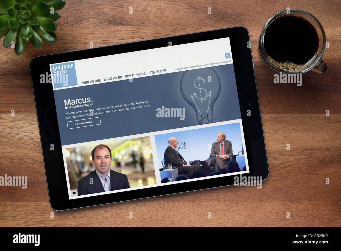 The website of Goldman Sachs is seen on an iPad tablet, on a wooden table along with an espresso coffee and a house plant (Editorial use only). Stock Photo