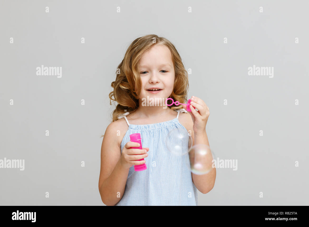 Portrait of a happy smiling little blonde girl on a gray background. Child blowing bubbles Stock Photo