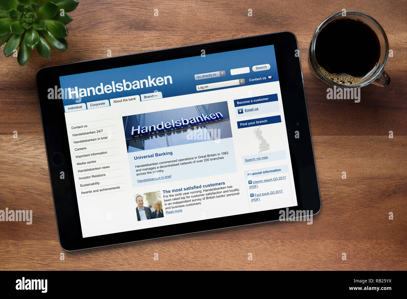 The website of Handelsbanken is seen on an iPad tablet, on a wooden table along with an espresso coffee and a house plant (Editorial use only). Stock Photo