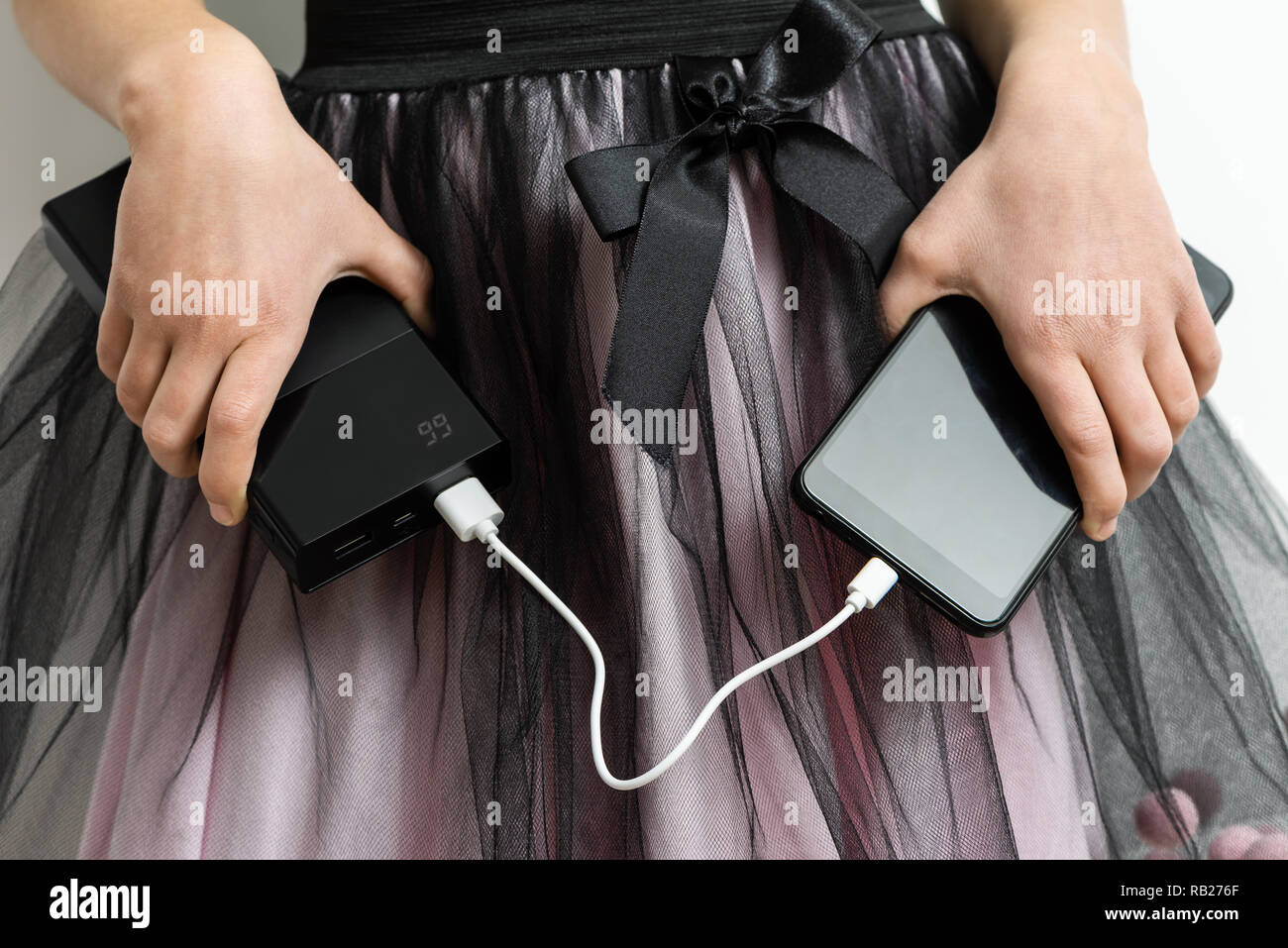 A girl is holding a smartphone and a power bank on the background of the skirt. Stock Photo