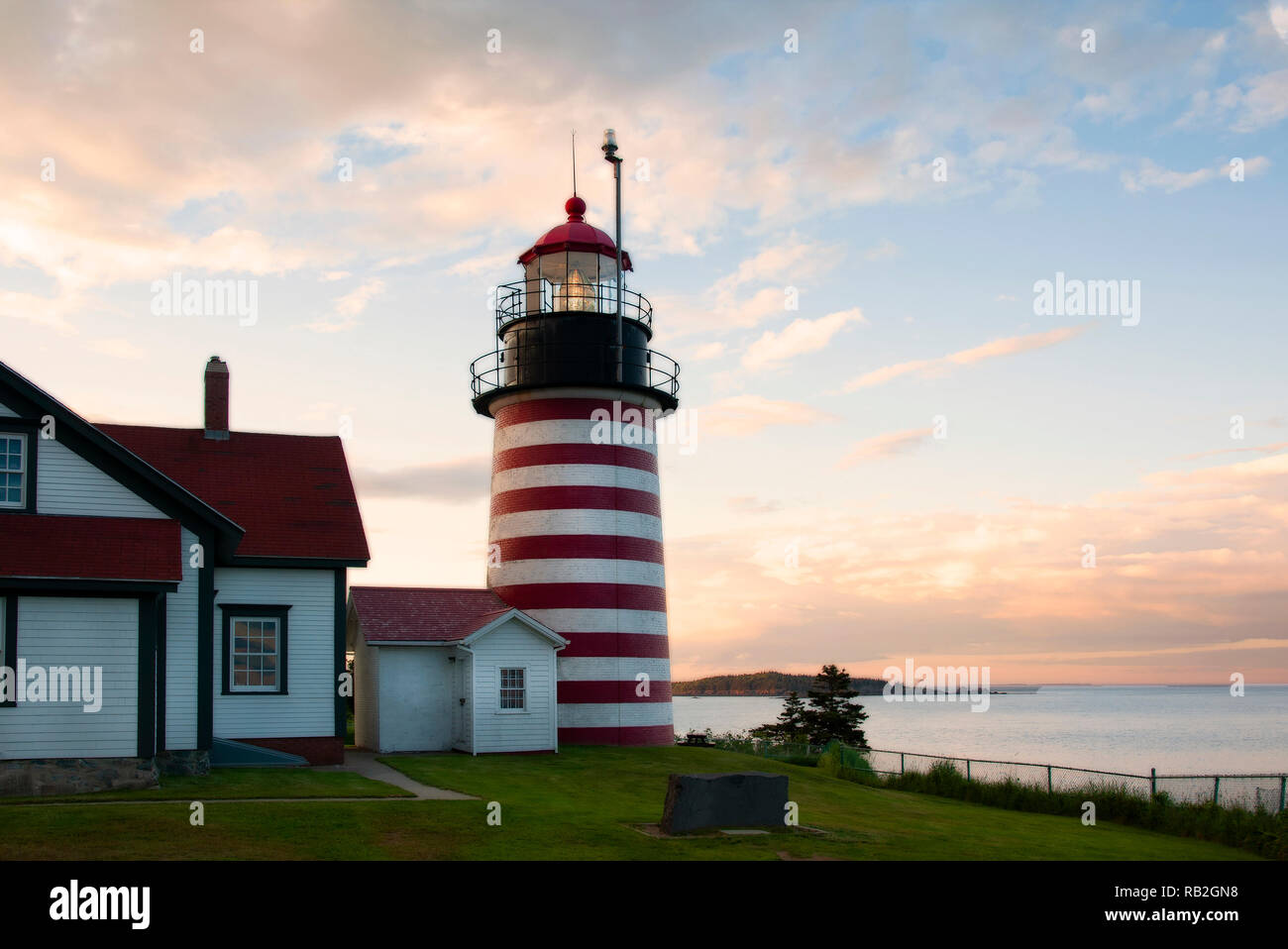 Old striped lighthouse tower of West Quoddy Head light shines brightly during sunset in northern New England. It uses an authentic Fresnel lens and is Stock Photo