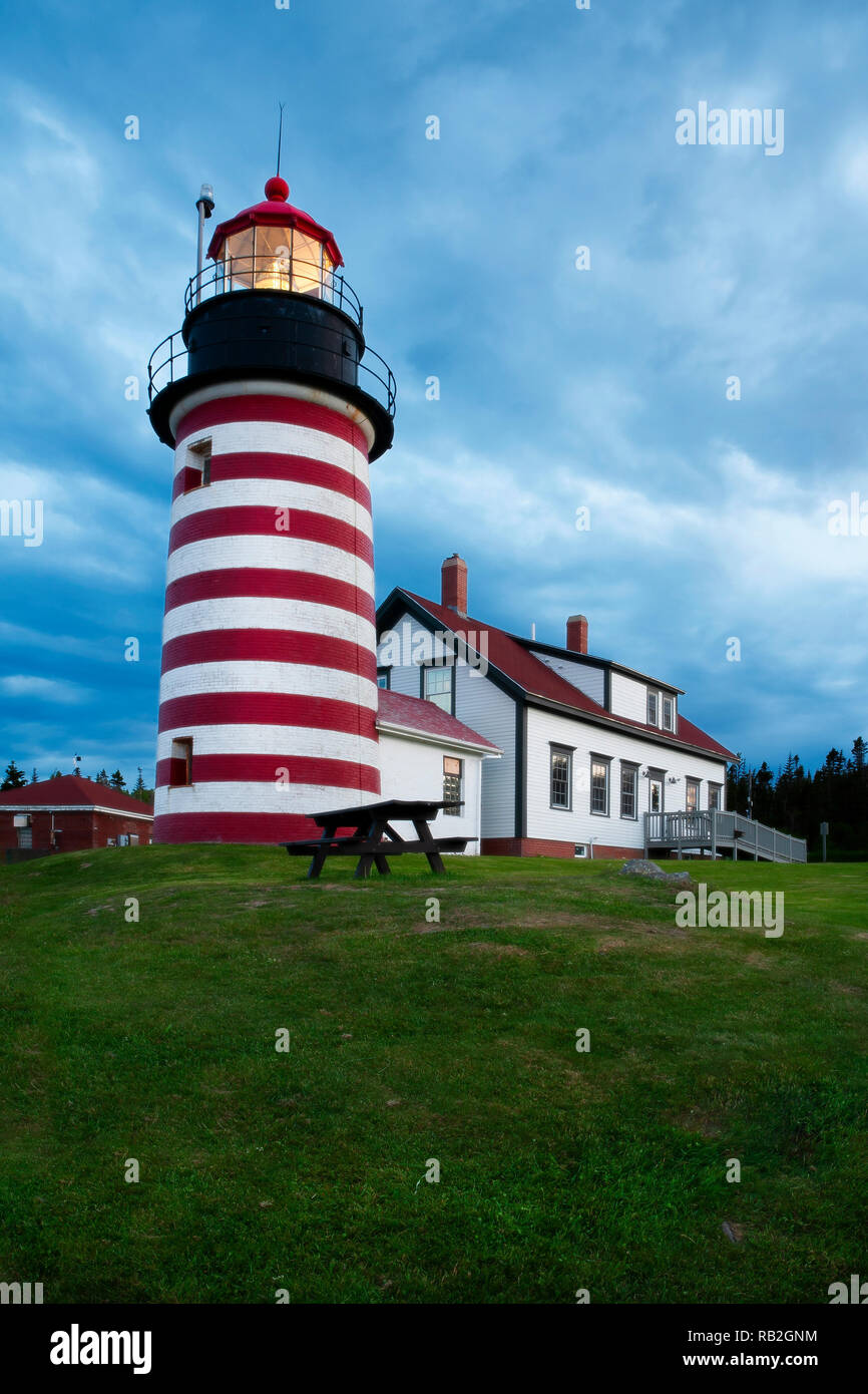 Storm clouds gather as light shines brightly of West Quoddy Head lighthouse, a red and white striped beacon in northern Maine, in New England. Tower s Stock Photo