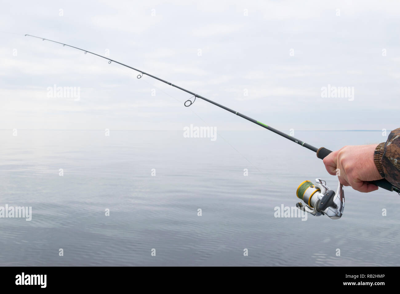 Hands of a fisherman with a spinning rod with the line with a line on a motor boat in the lake on a cloudy day Stock Photo