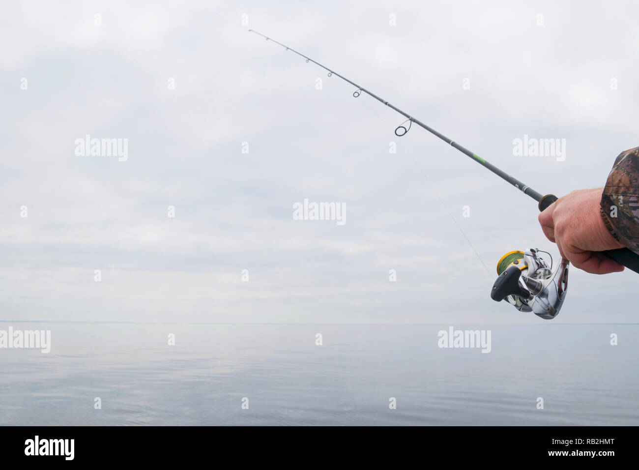 Hands of a fisherman with a spinning rod with the line with a line on a motor boat in the lake on a cloudy day Stock Photo
