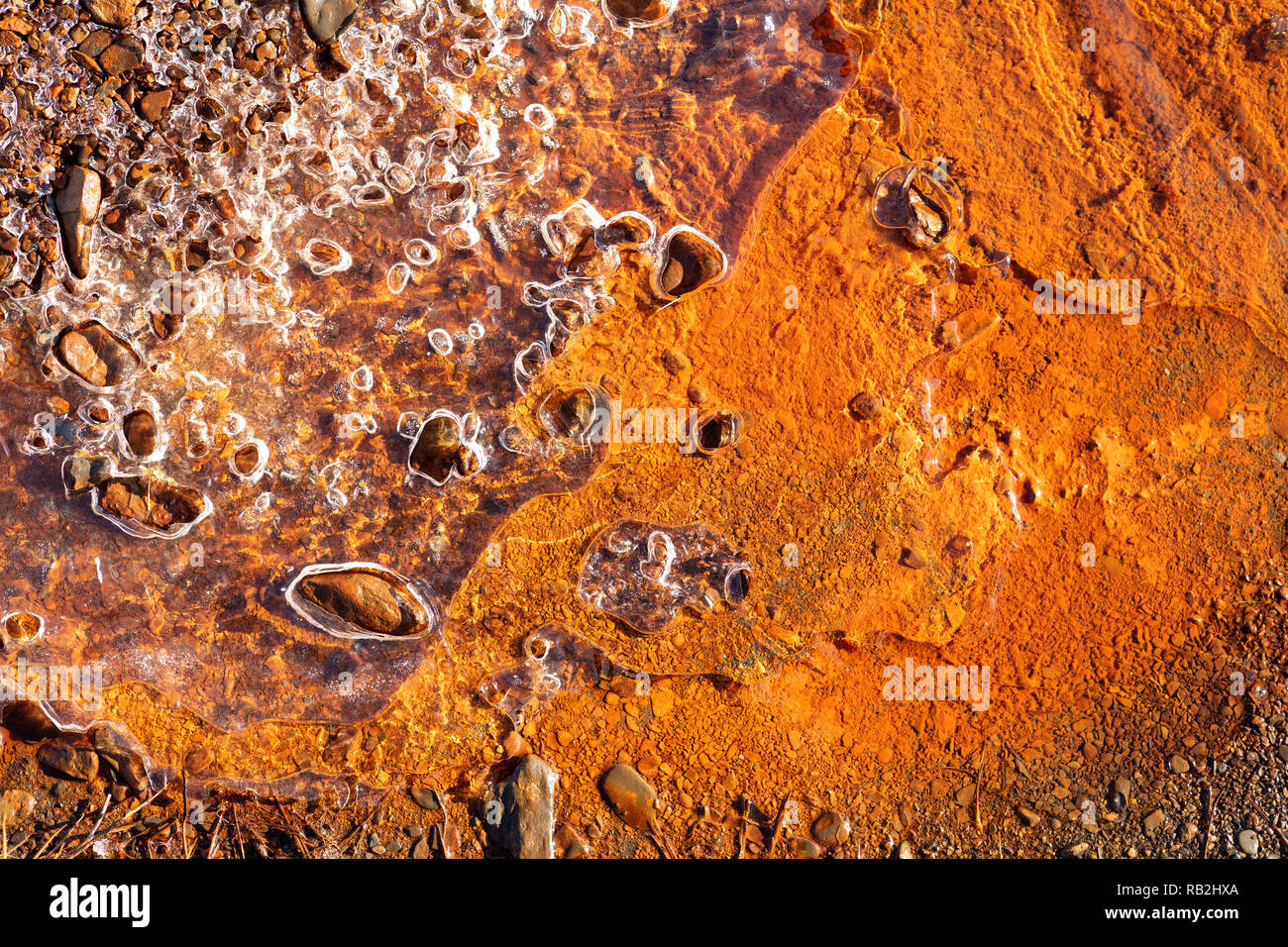 rusty orange background under a sheet of frozen water, some stones protude from the transparent ice sheet Stock Photo