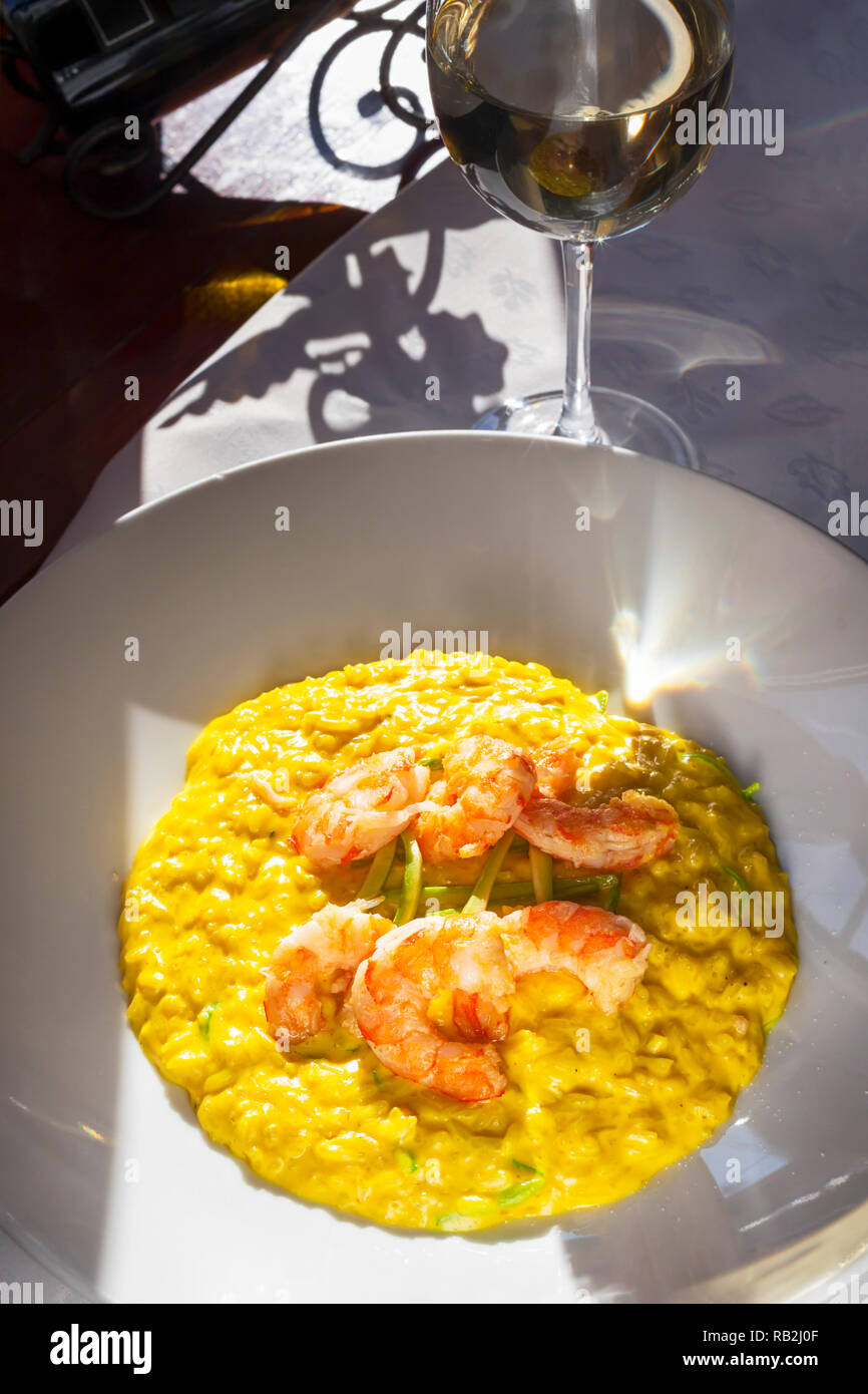 Sunlit plate of king prawns with saffron rice and zucchini - Paella Valenciana served with glass of white wine Stock Photo