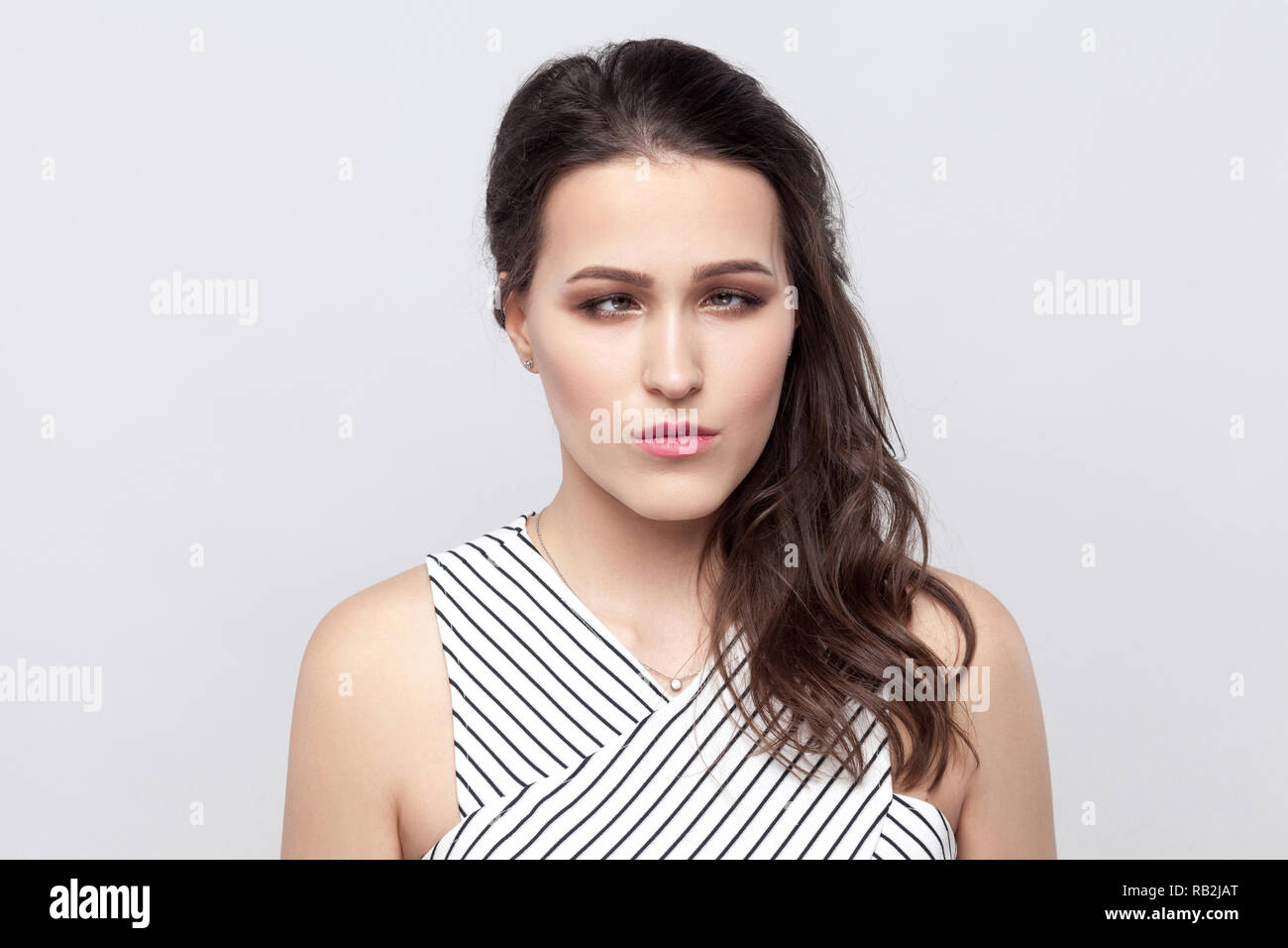 Portrait of crazy funny beautiful young brunette woman with makeup and striped dress standing and looking at camera with crossed eyes. indoor studio s Stock Photo