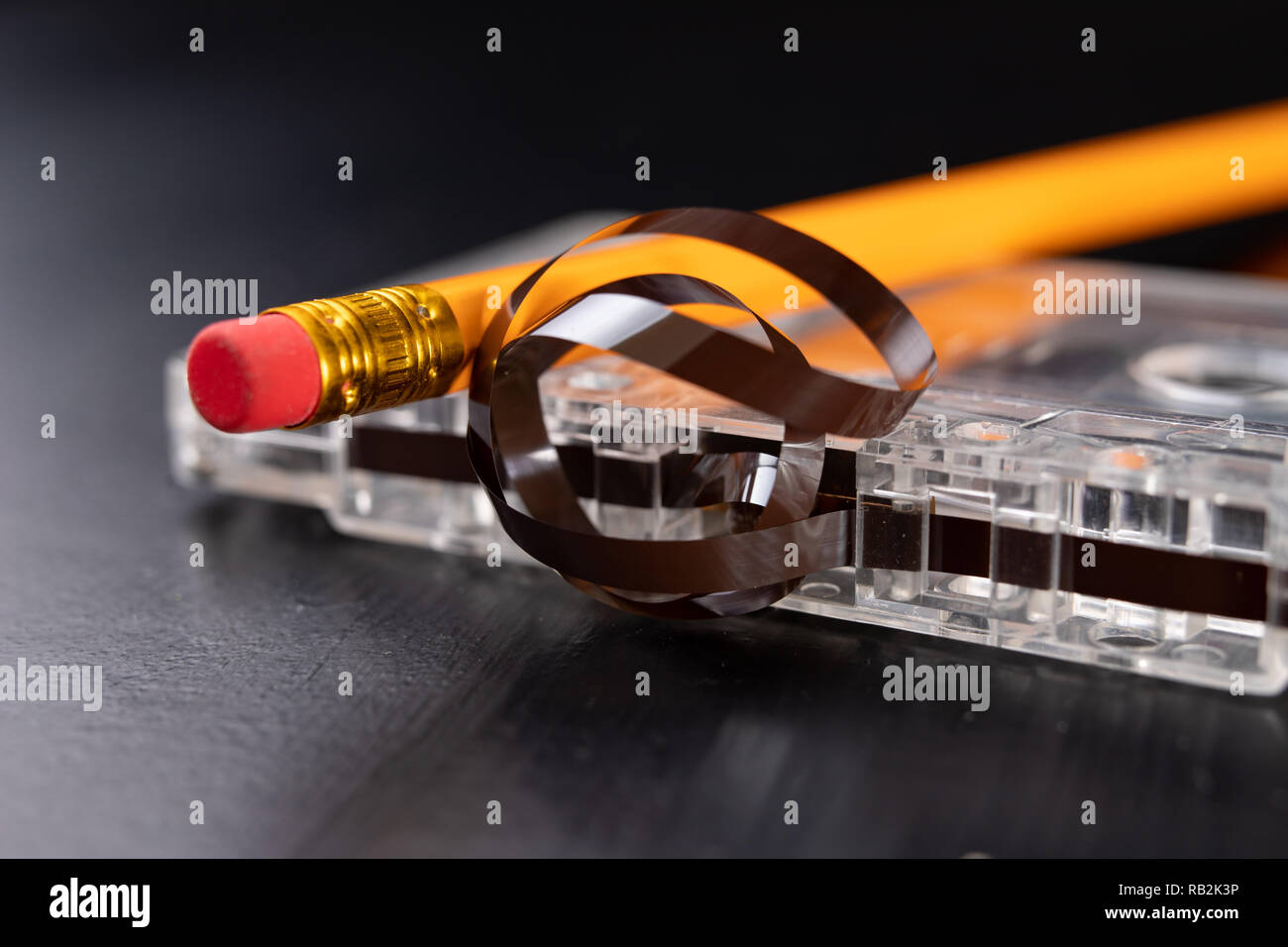 Audio cassette and pencil on a black table. Old data carrier. Dark background Stock