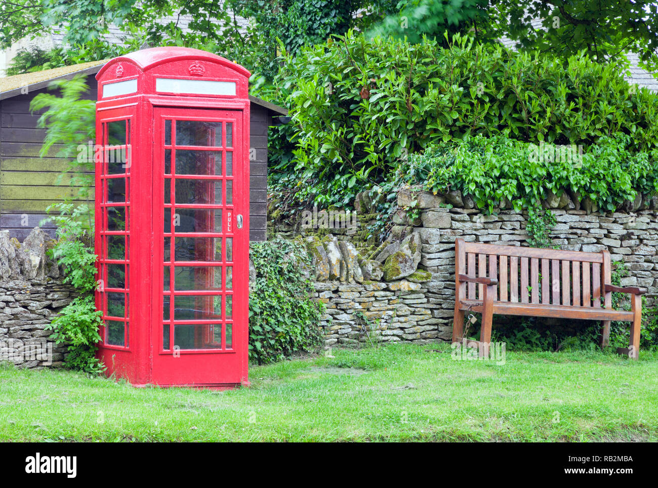 Red classic telephone box by a wooden bench in a village common, English rural countryside Stock