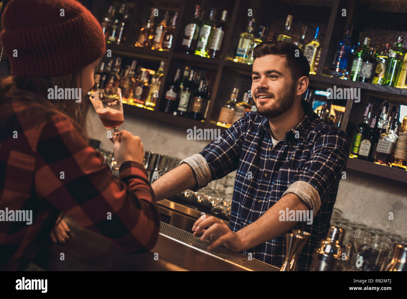 Young barman standing at bar counter talking with girl drinking
