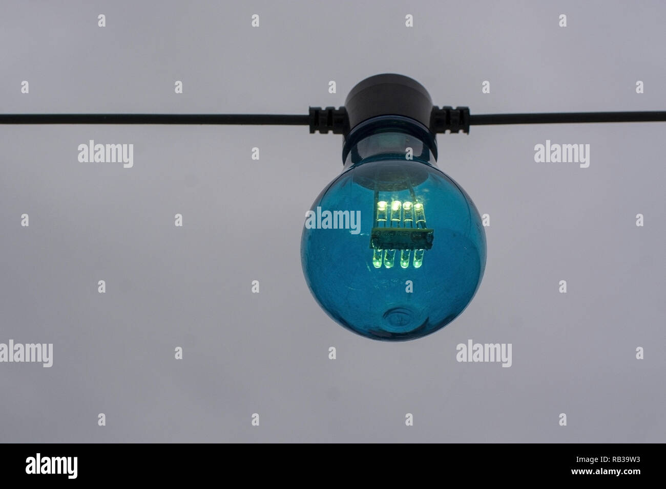 Blue color lightbulb on string against gray sky background Stock Photo