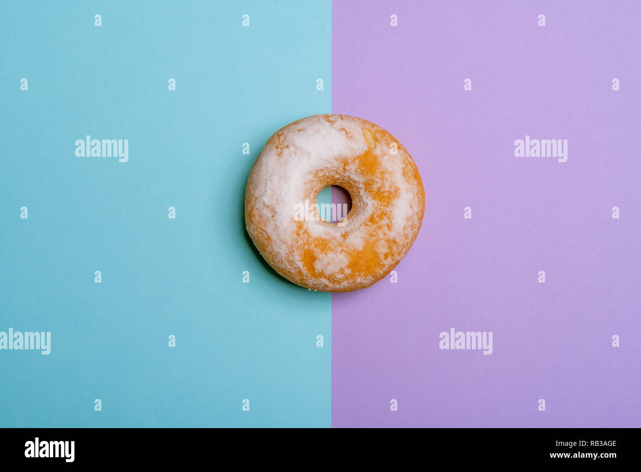 Round donut sugar powdered on a bicolored background, blue and magenta. Above view in minimalism style with copy space Stock Photo