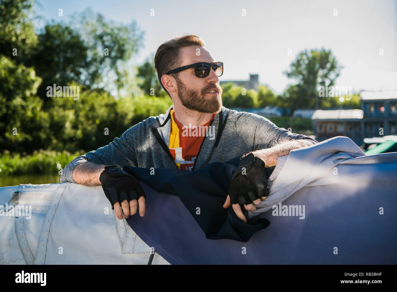 Handsome man traveling by yacht. Casual outfit, man dressed in grey hoodie, spring time, bearded man in sunglasses on the boat. Stock Photo