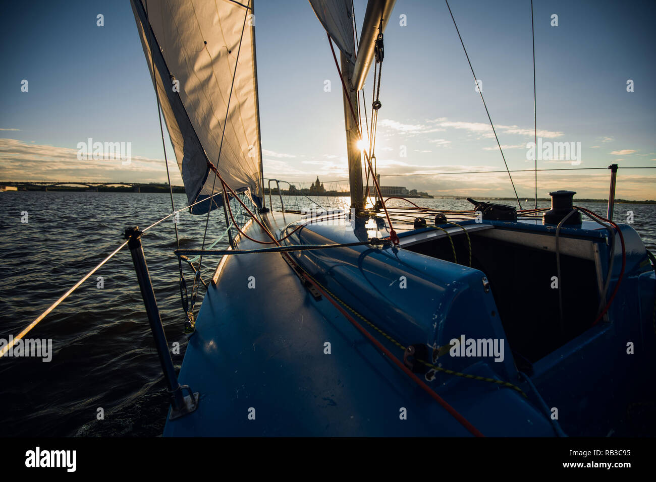 Sunset at the Sailboat deck while cruising sailing at opened sea or river. Yacht with full sails up at the end of windy day. Sailing theme - background. Yachting background design. Stock Photo