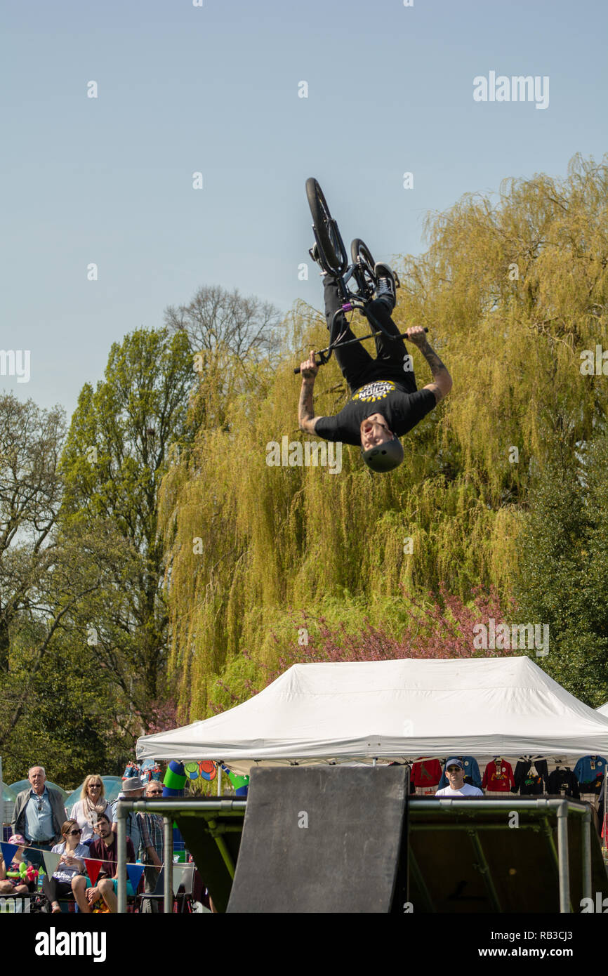 BMX rider performs stunts at country fair, gets lots of air, against a background of trees Stock Photo