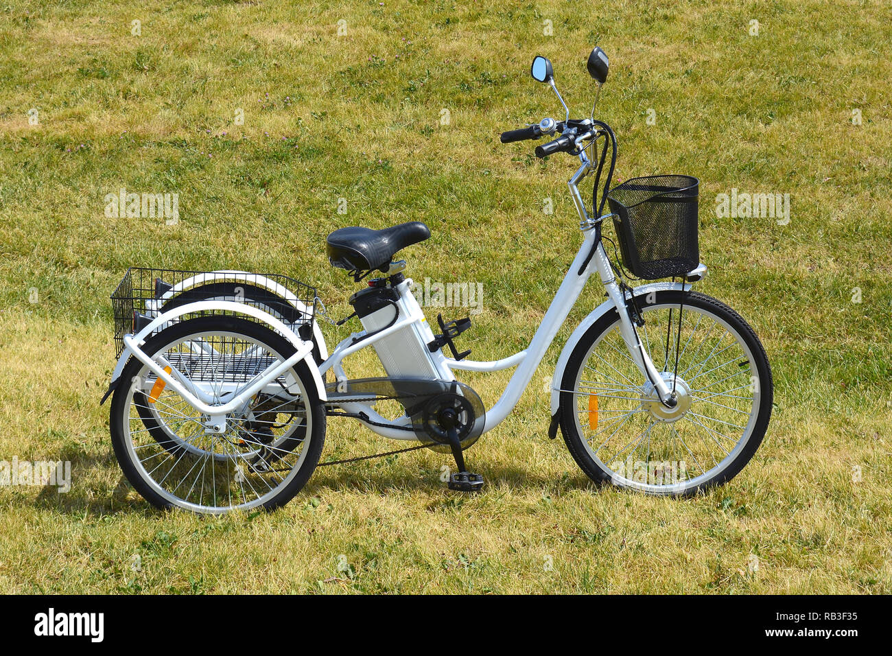 Electric trike or bicycle in the park in sunny summer day. Shot from the side. Unfiltered natural lighting. The view of the e motor and power battery. Stock Photo