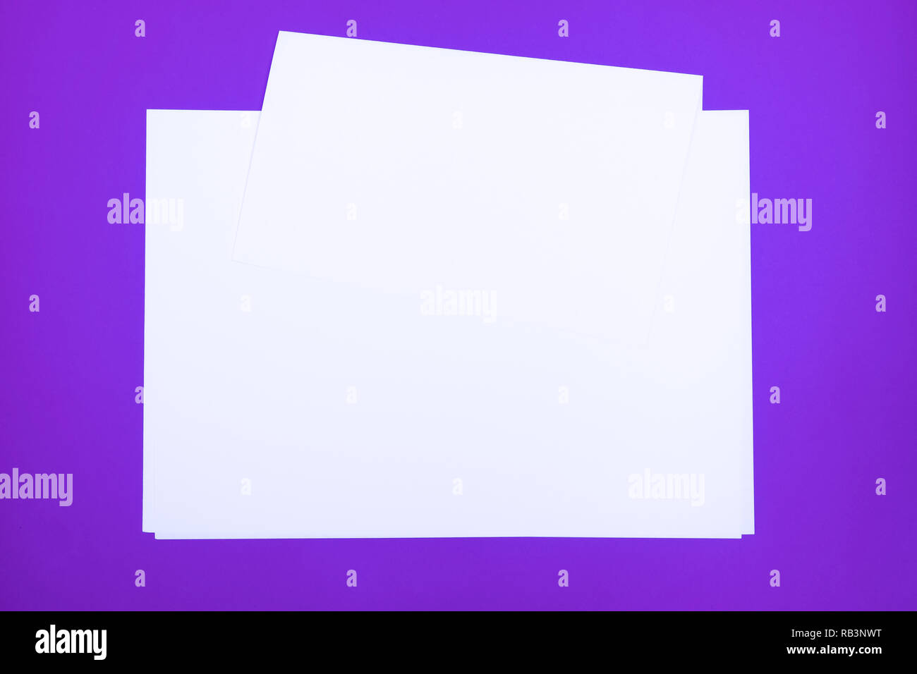 Blank paper sheets on 'proton purple' background. Top view of white paper laying on bright colored table top Stock Photo