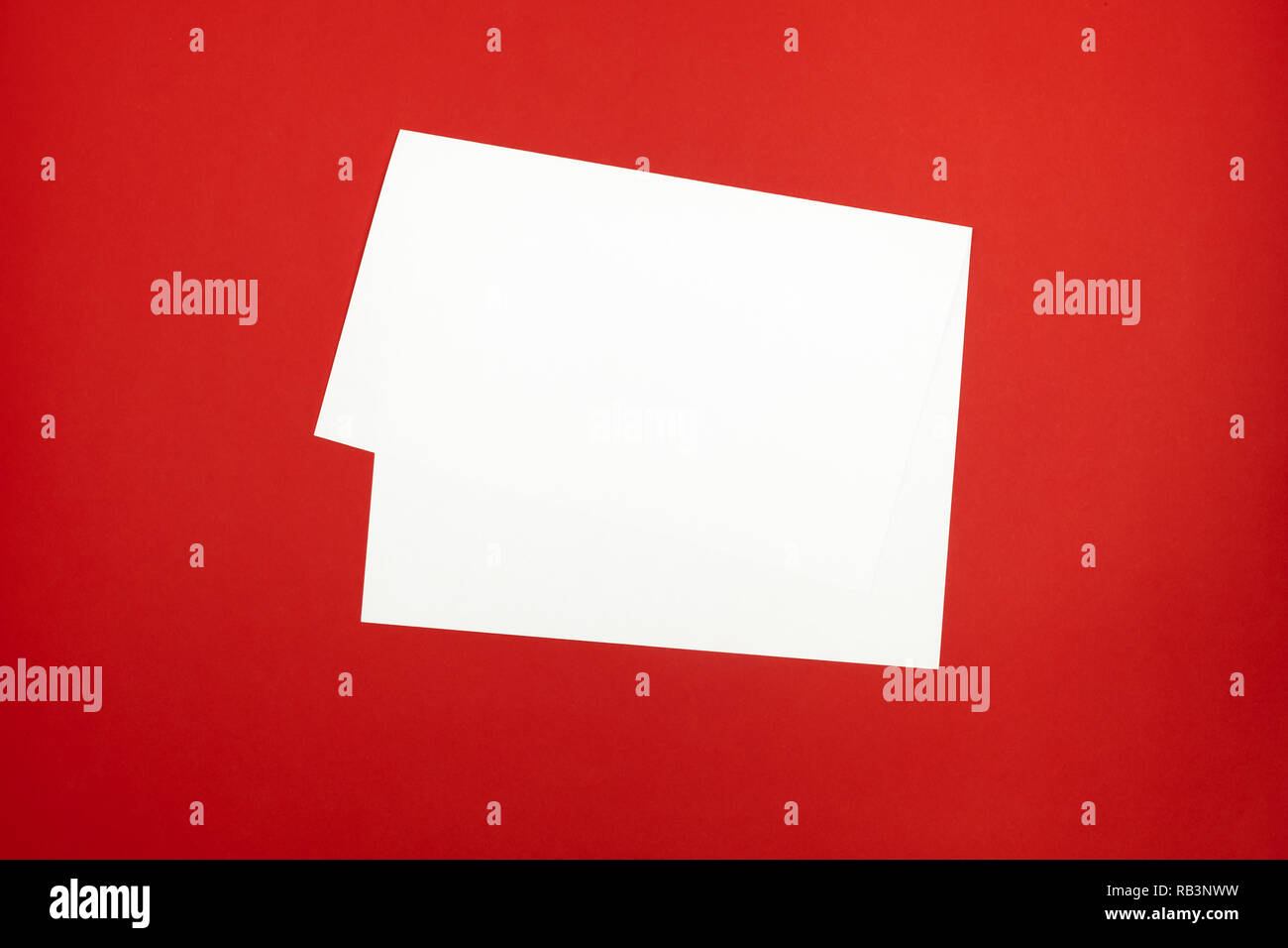 Blank paper sheet on bright red background. Top view of bent white paper laying on vivid colored table top Stock Photo
