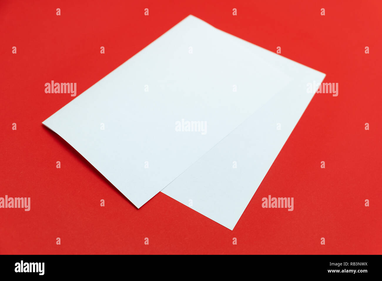 Blank paper sheet on bright red background. Close-up view of bent white paper laying on vivid colored table top Stock Photo