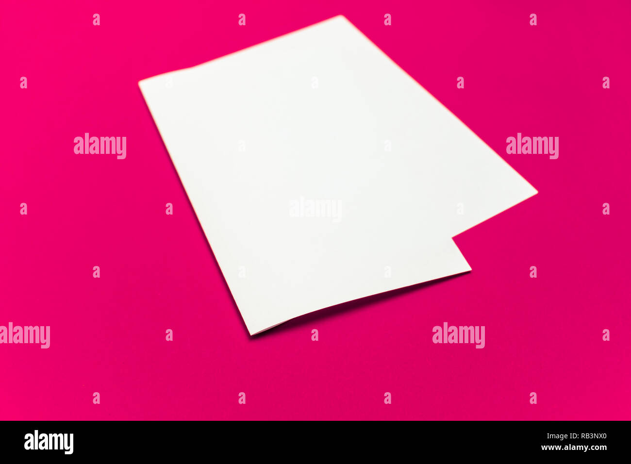 Blank paper sheet on 'plastic pink' colored background. Close-up view of bent white paper laying on bright table top Stock Photo