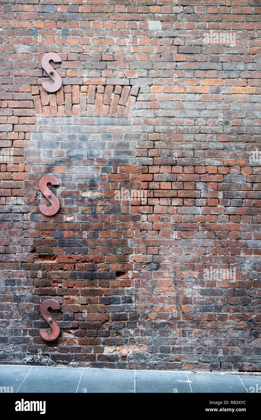 Old brick wall along a sidewalk with three Sshaped wall braces