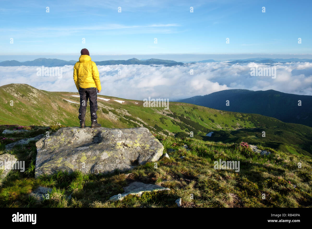 Alone tourist in yellow jacket stay on rock on high mountains. Stock Photo